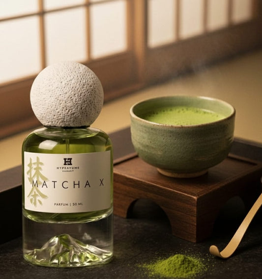 Bottle of Matcha X perfume next to a bowl of matcha tea on a wooden surface.