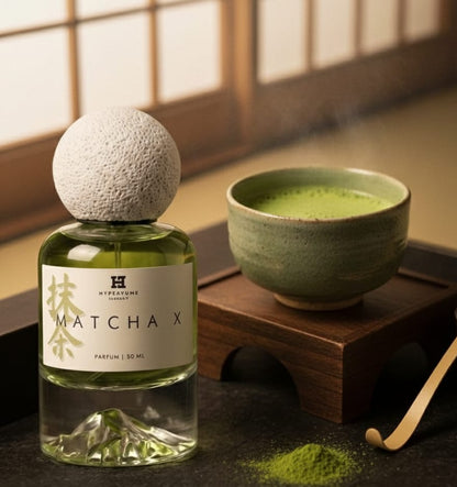 Bottle of Matcha X perfume next to a bowl of matcha tea on a wooden surface.